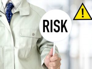「RISK」のプレートを掲げる作業服姿の男性